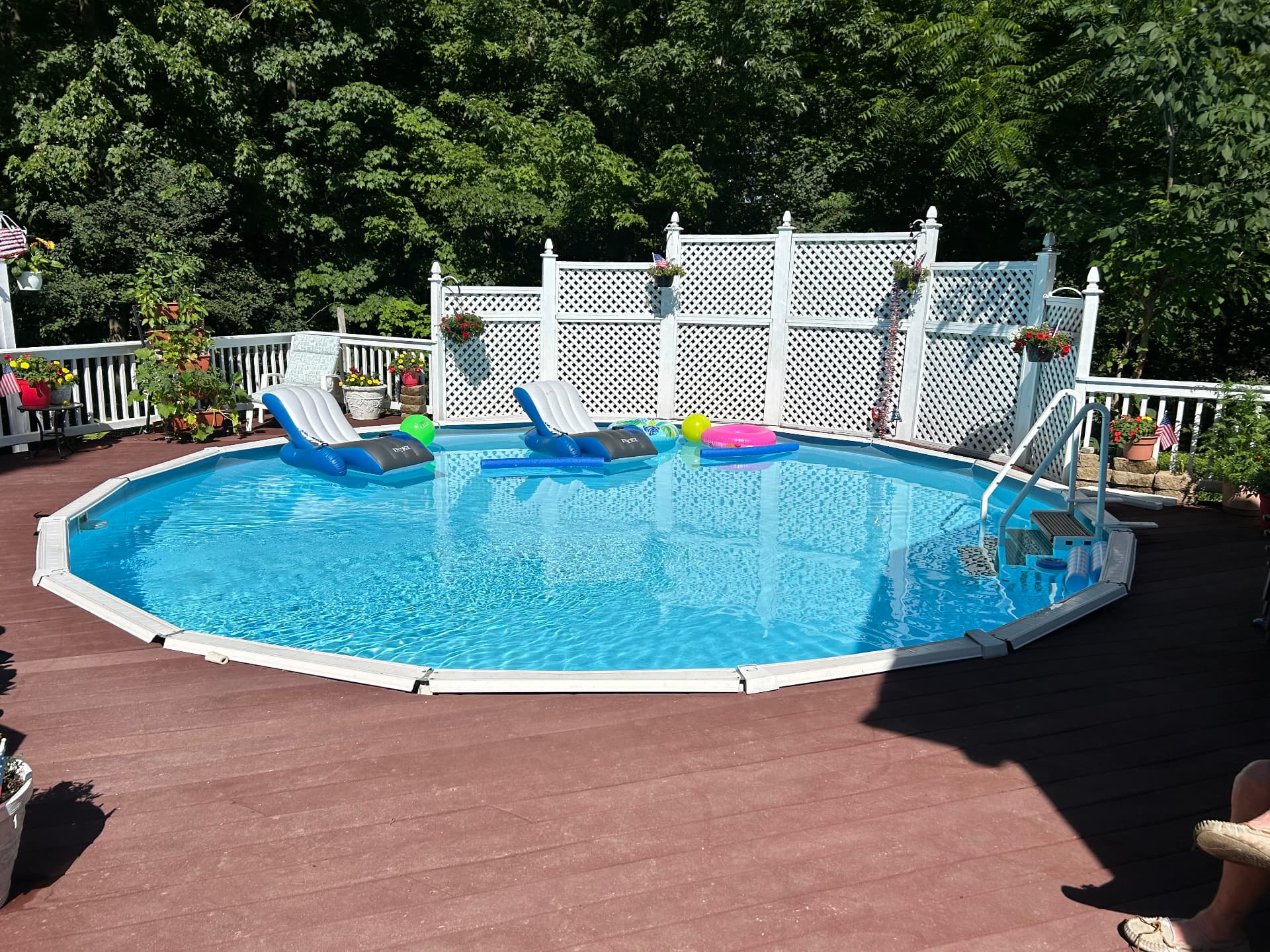 After: above-ground pool surrounded by composite deck, railings and white lattice privacy fence